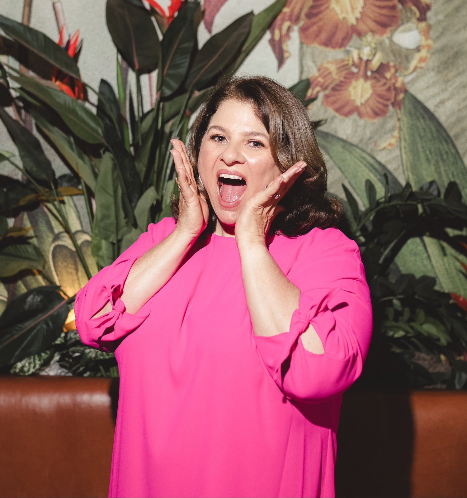 Samantha smiles with an excited expression, hands framing her face, while standing in front of a colorful tropical mural as the featured Eyece Breaker storyteller.
